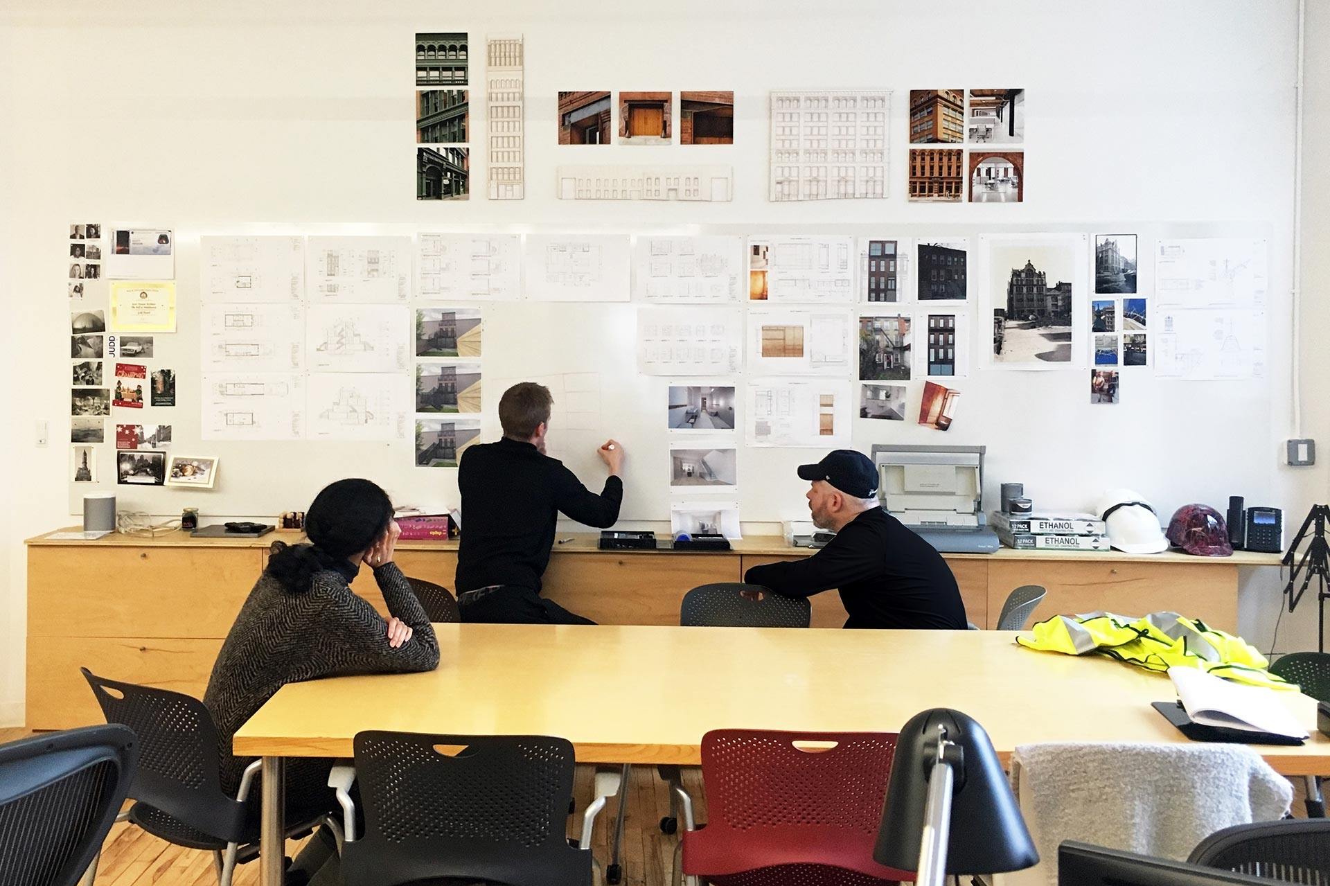 two people sitting at a table in front of a whiteboard