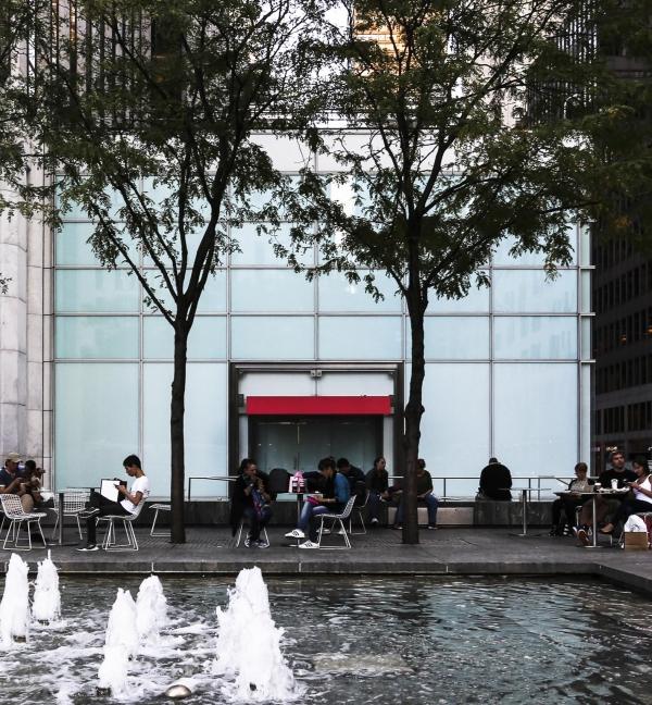 people sitting at tables near a fountain in front of a building