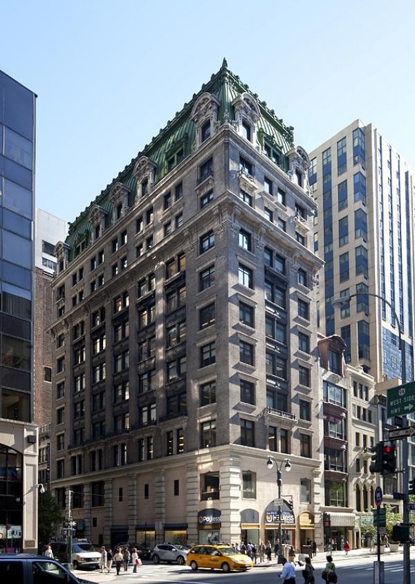 a tall building with a green roof on the corner of a street