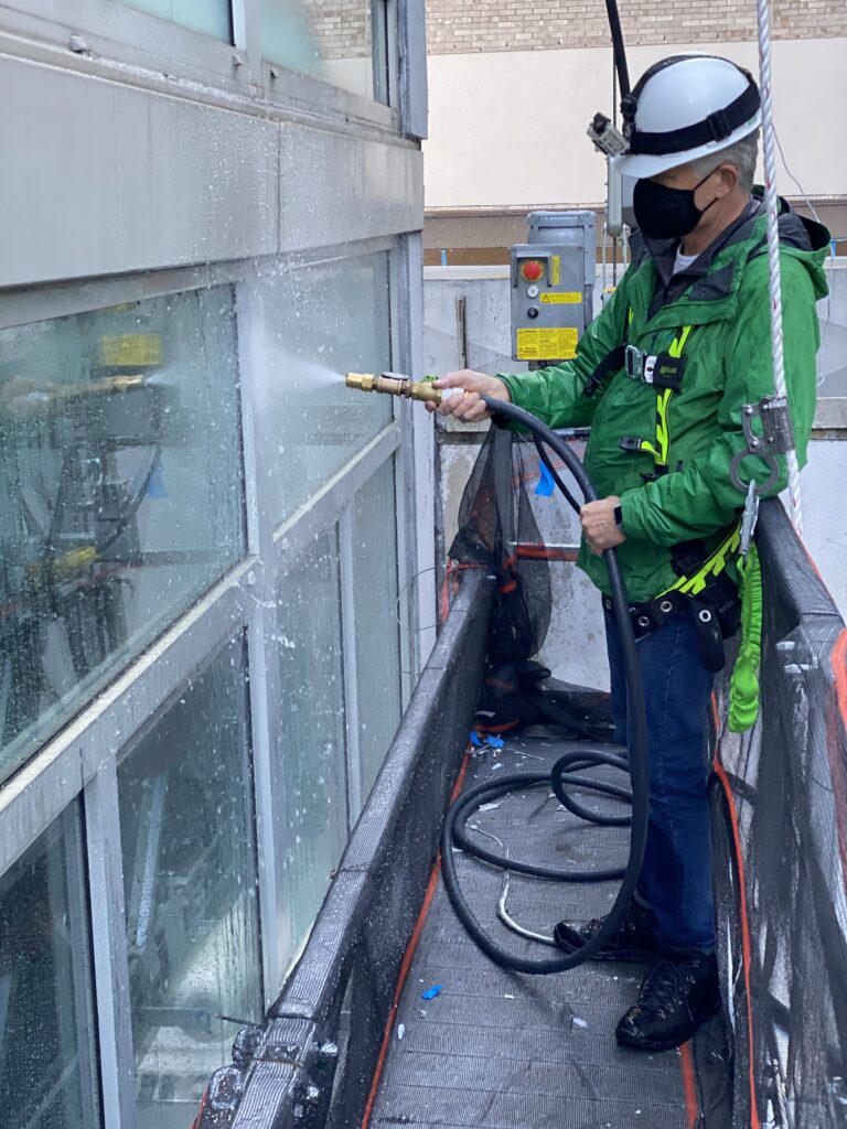 a man in green jacket spraying water on window