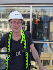 On-site photo of Matthew Radune in a white construction hat standing in front of a building