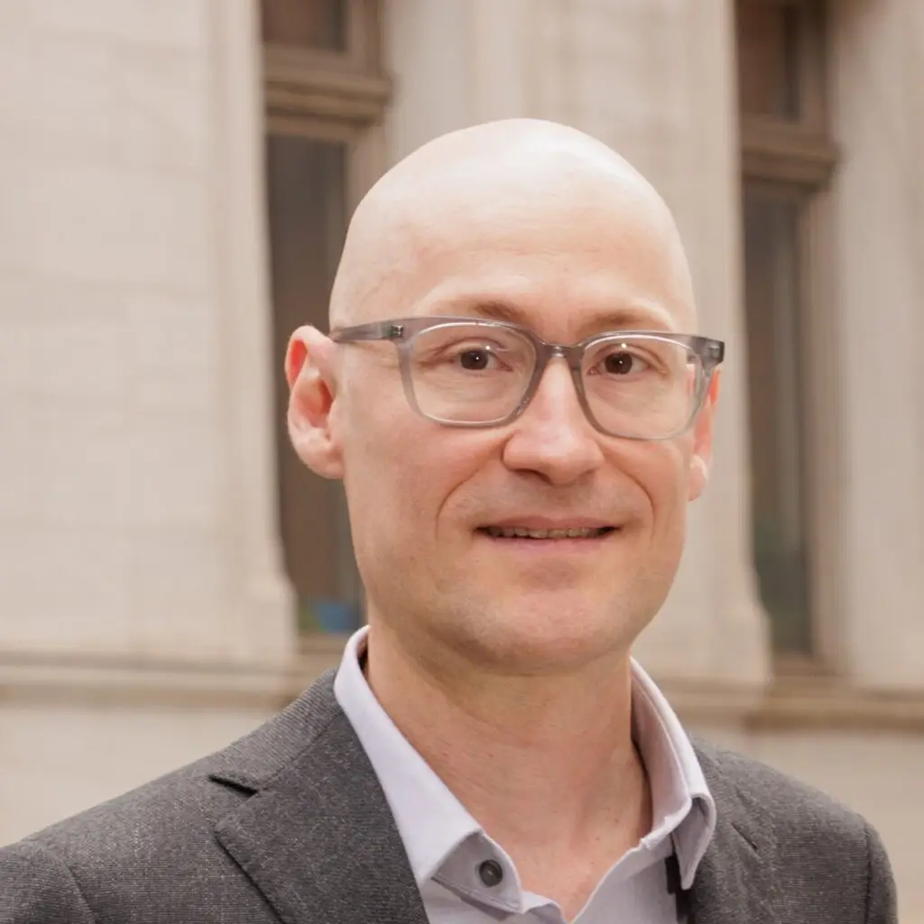 a bald man wearing glasses standing in front of a building